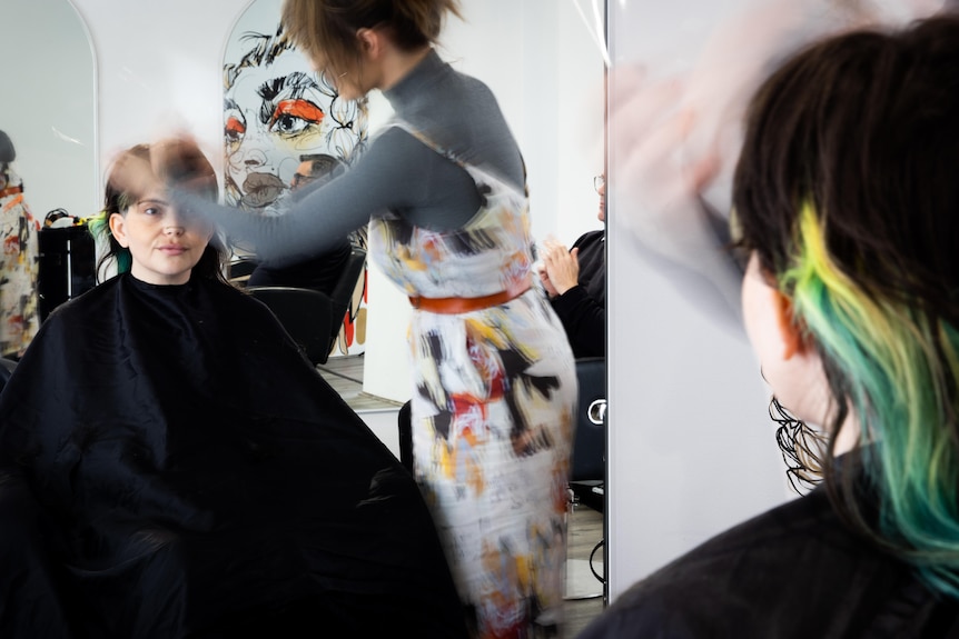 A client looking into the mirror while a hairstylist cuts her hair.