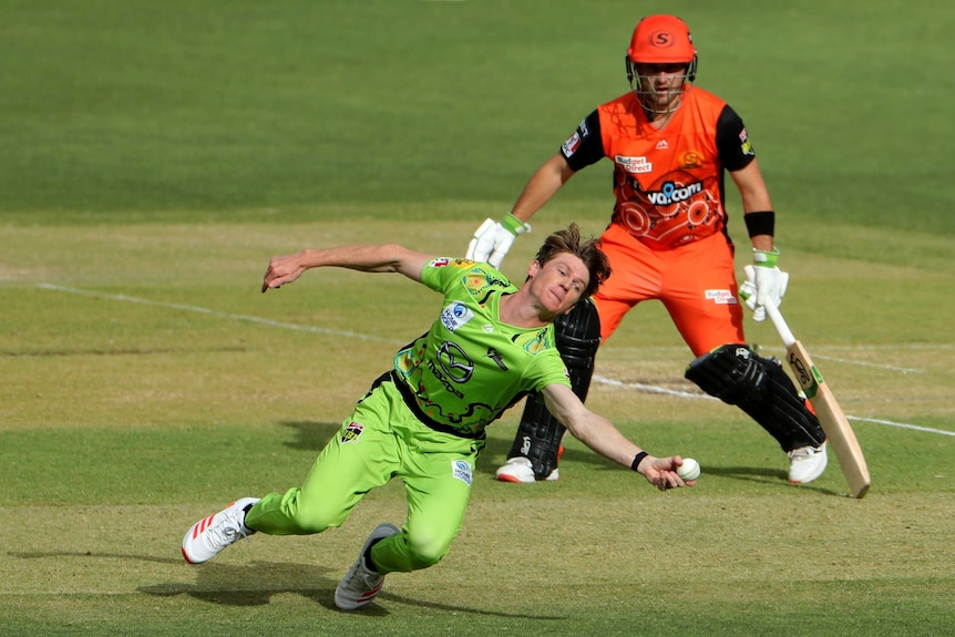 Brendan Doggett dives and clutches on to the ball as a Scorchers batsman looks on.