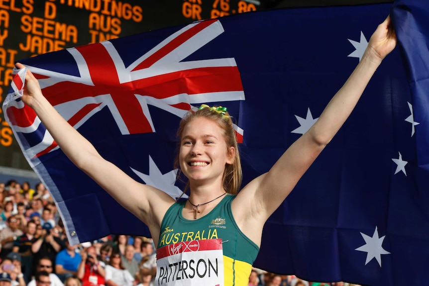 A female high jumper holds the Australian flag behind her head as she celebrates a Commonwealth Games gold medal in 2014.