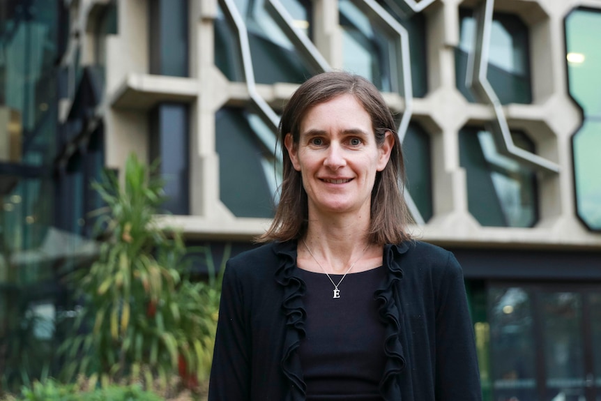 A woman with shoulder length hair in front of a modern building.