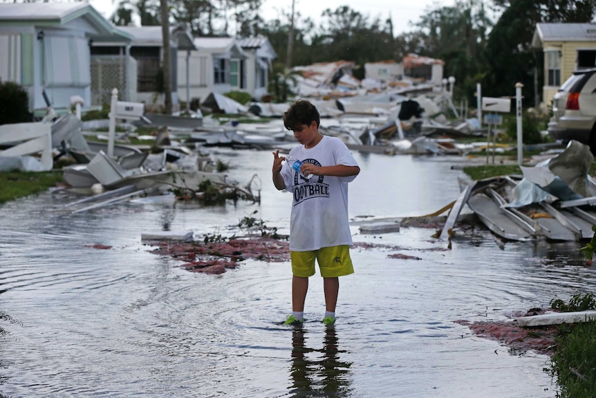 A boy stands in the middle of a street littered with debris.