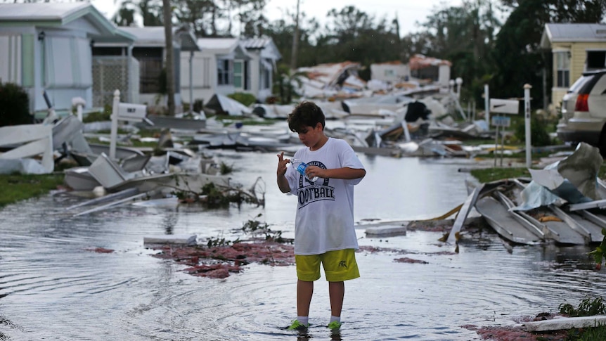 A boy stands in the middle of a street littered with debris.