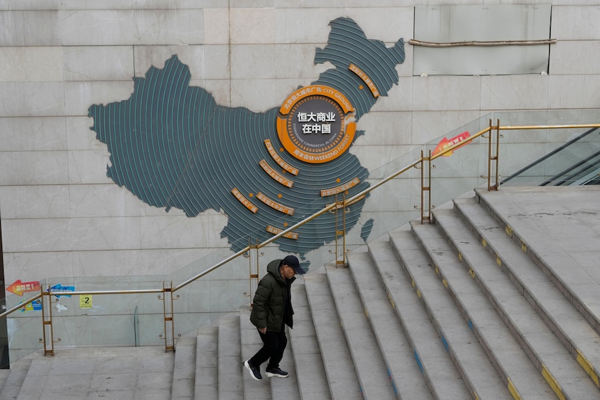 A man walks up cement steps past a map on a wall 