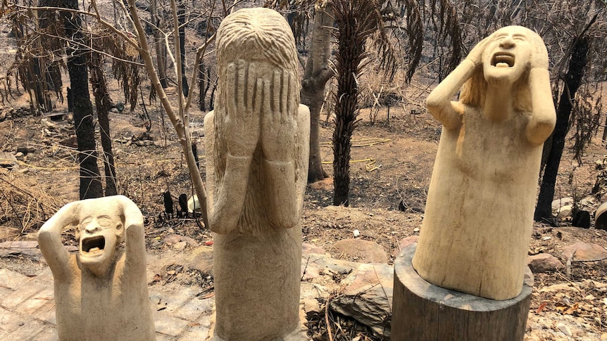 Statues showing people screaming and clutching at their face in despair, standing in burnt landscape.