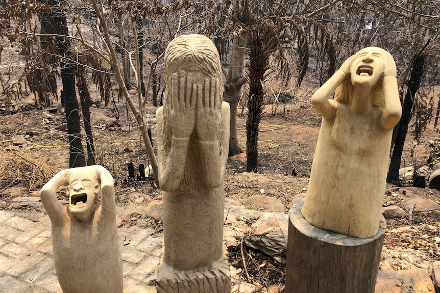 Statues showing people screaming and clutching at their face in despair, standing in burnt landscape.