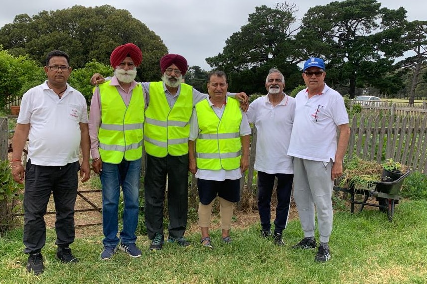 Members of Club 60 Tarneit stand near a garden in high-vis vests. 