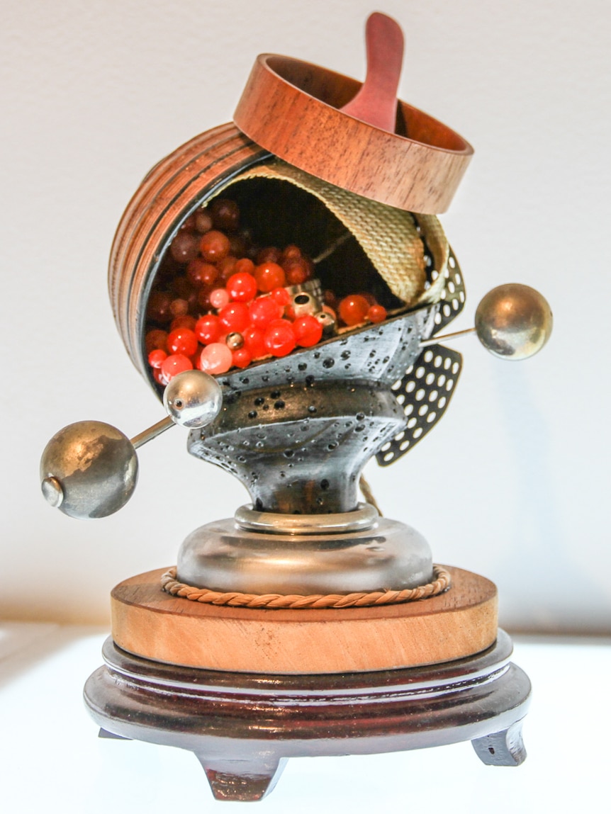 An artwork using metal, wood and small red balls.