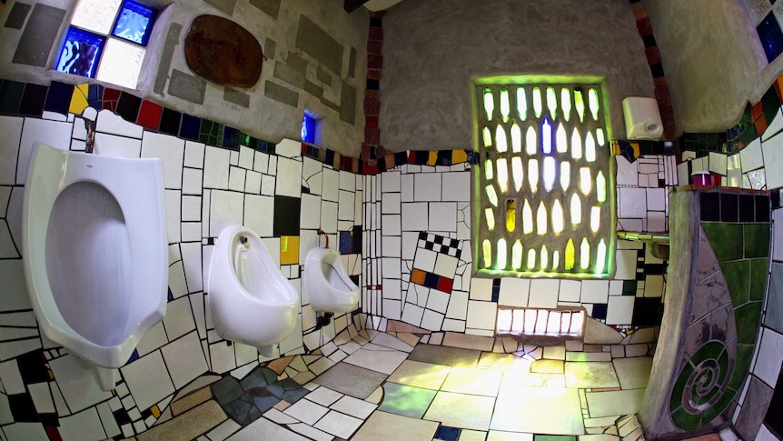 A shot of an interior a surreal public toilet: multi-coloured tiles, odd angles and coloured glass abound.