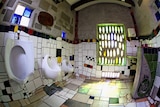 A shot of an interior a surreal public toilet: multi-coloured tiles, odd angles and coloured glass abound.