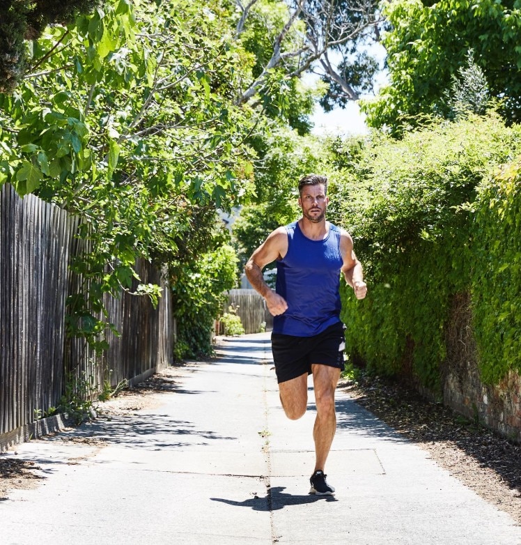 A man in a blue singlet and black shorts jogging on a path