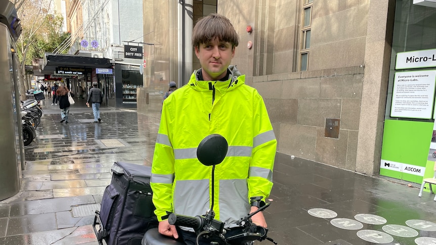 Davis Clayton in a high vis jacket standing on a city street with his motorbike