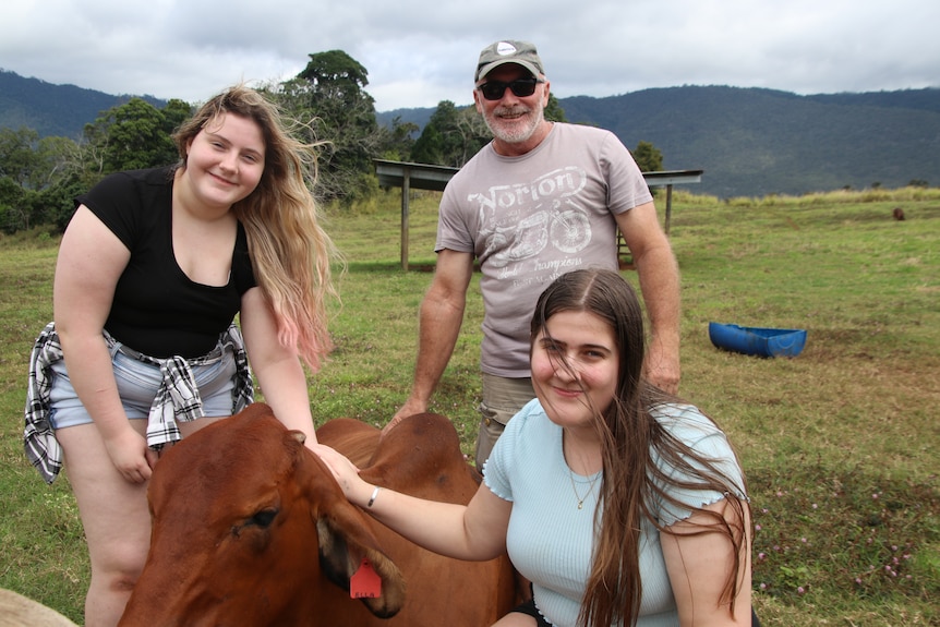 Father and two daughters standing next to a sitting brown cow