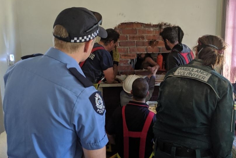 A boy's arm is supported through a hole cut in the wall to get him out of the chimney.