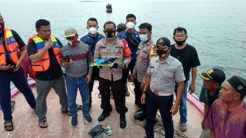 A police officer on a boat holding debris with other men and officials surrounding him.