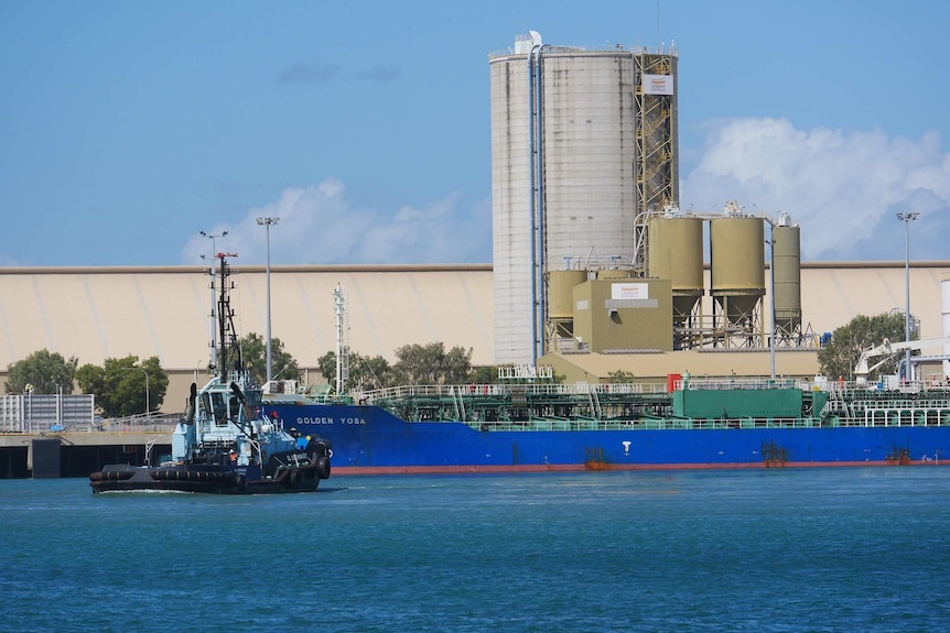 A freight ship docked in the Port of Townsville with a tug boat in the foreground and silos in the background