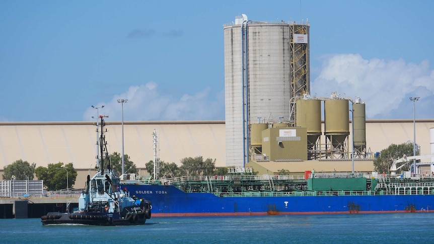 A freight ship docked in the Port of Townsville with a tug boat in the foreground and silos in the background