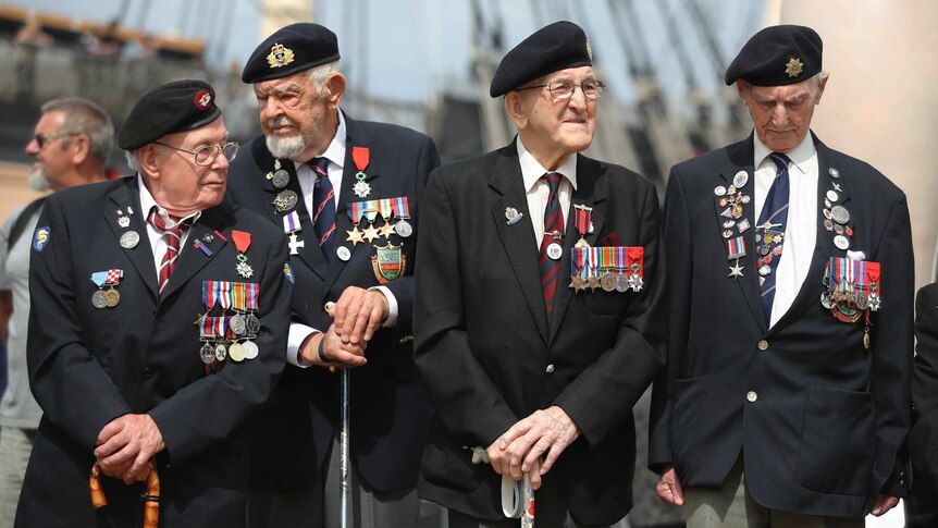 D-Day veterans stand with canes wearing war medals.