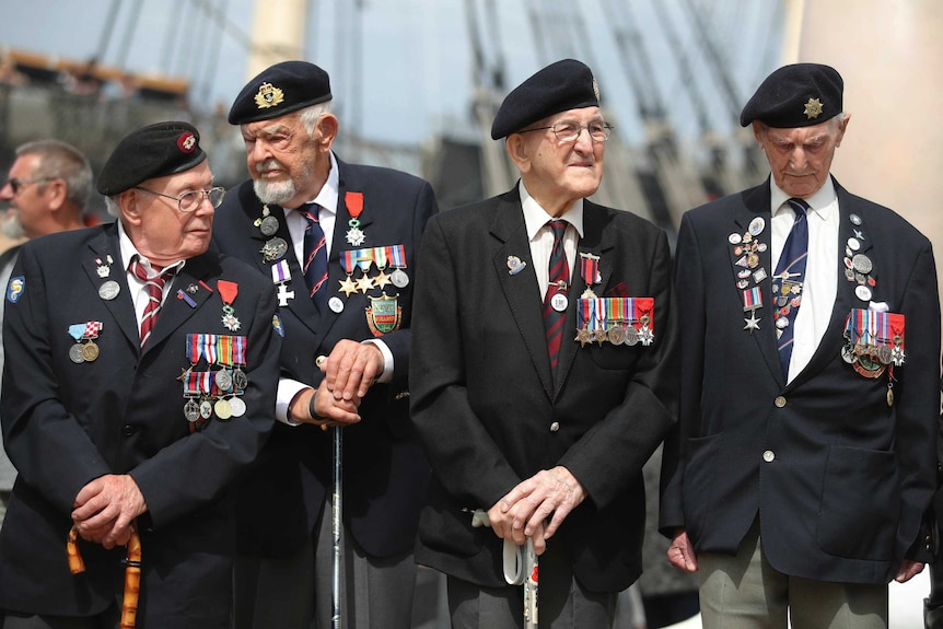 D-Day veterans stand with canes wearing war medals.