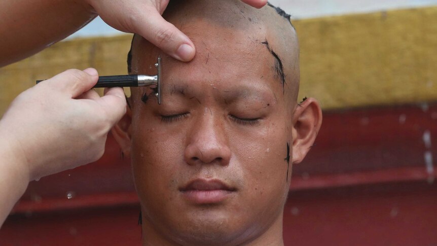 Coach Ekkapol Chantawong has his eyebrows shaved in the traditional ceremony.