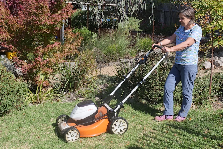 A woman pushing a lawnmower.