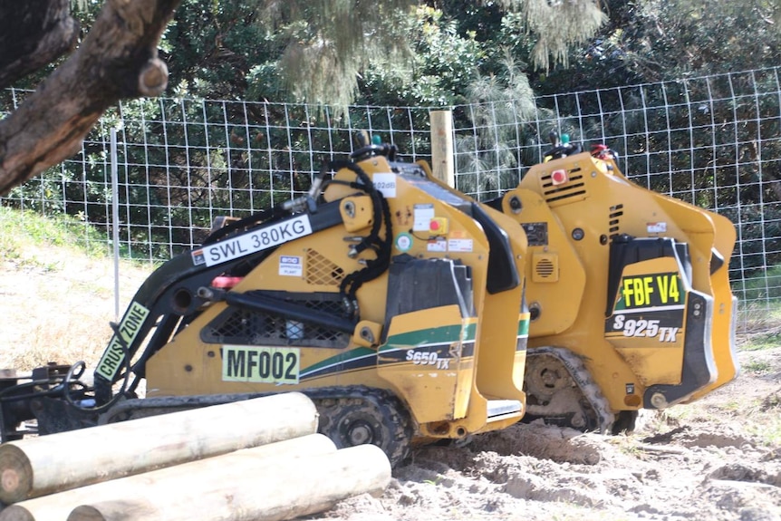 Two excavators on a beach building a dingo fence around a beachfront campsite on Fraser Island.