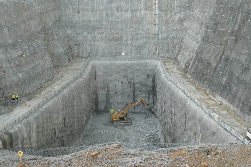 A large excavator in a deep, steep-sided grey pit.