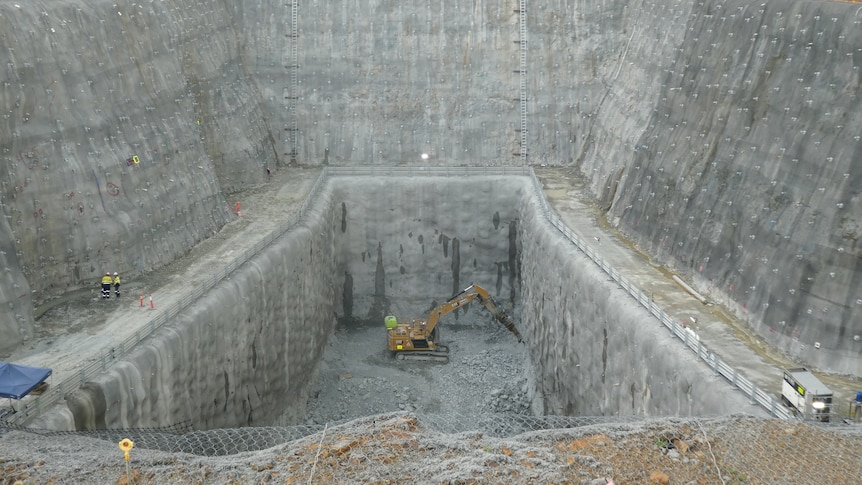 A large excavator in a deep, steep-sided grey pit.