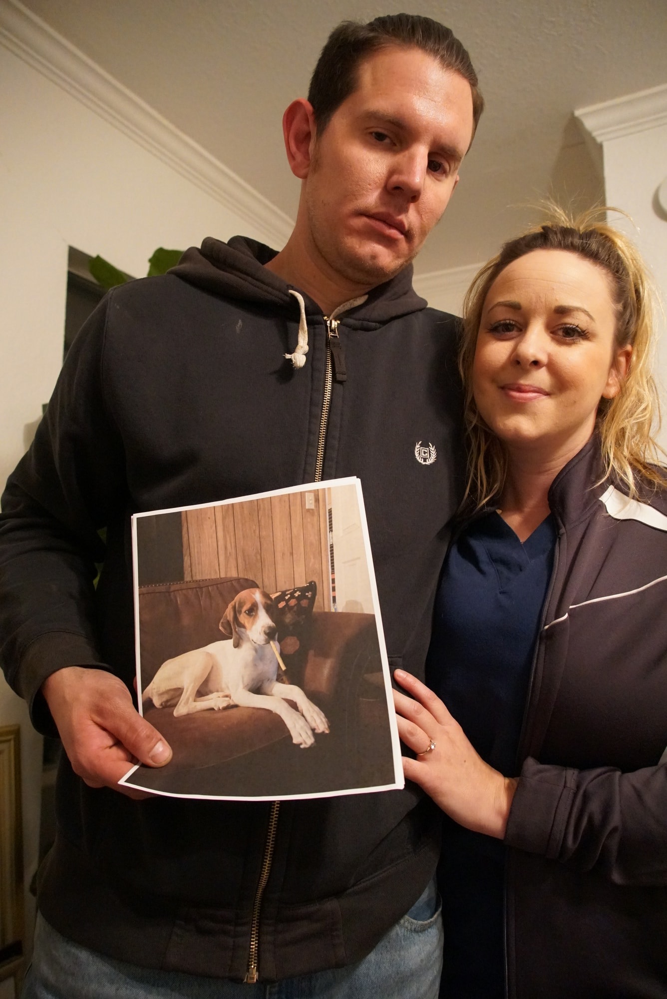 A couple looking devastated hold a photo of a dog