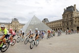 A large group of cyclists pedal past the historic structure of the Louvre museum. 