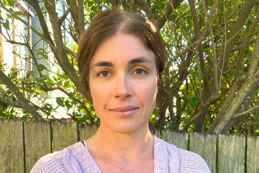 A medium shot of a woman with brown hair wearing a purple cardigan