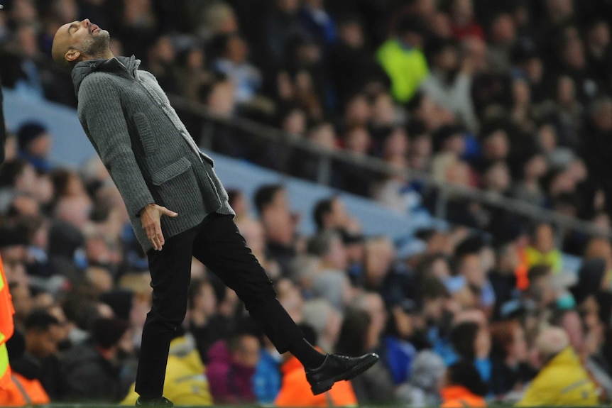 Pep Guardiola leans back standing on one let with his eyes closed with his face raised to the sky