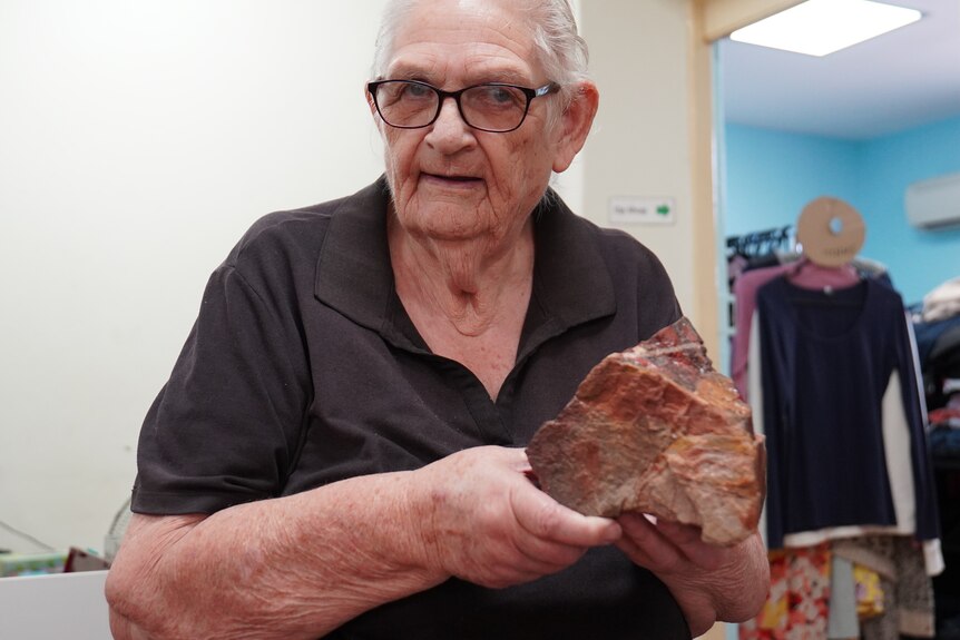 A woman in a black polo holds up a layered rock.