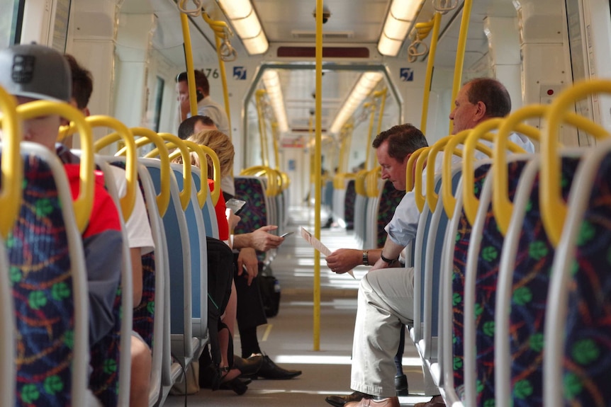 Long shot looking up a train carriage at Mark McGowan, seated reading a document.