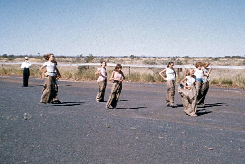 Children compete in a sack race on a blue asbestos track