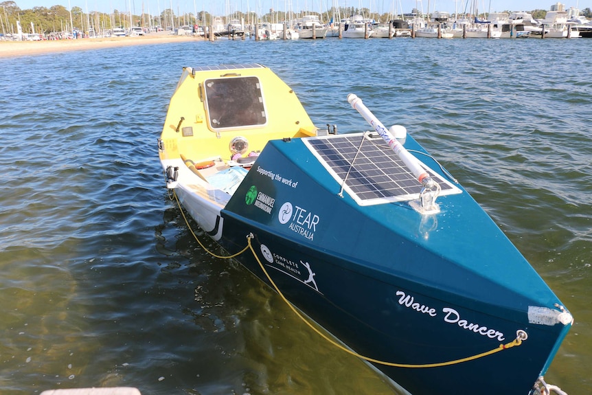 A blue and yellow boat in the water just off a beach.