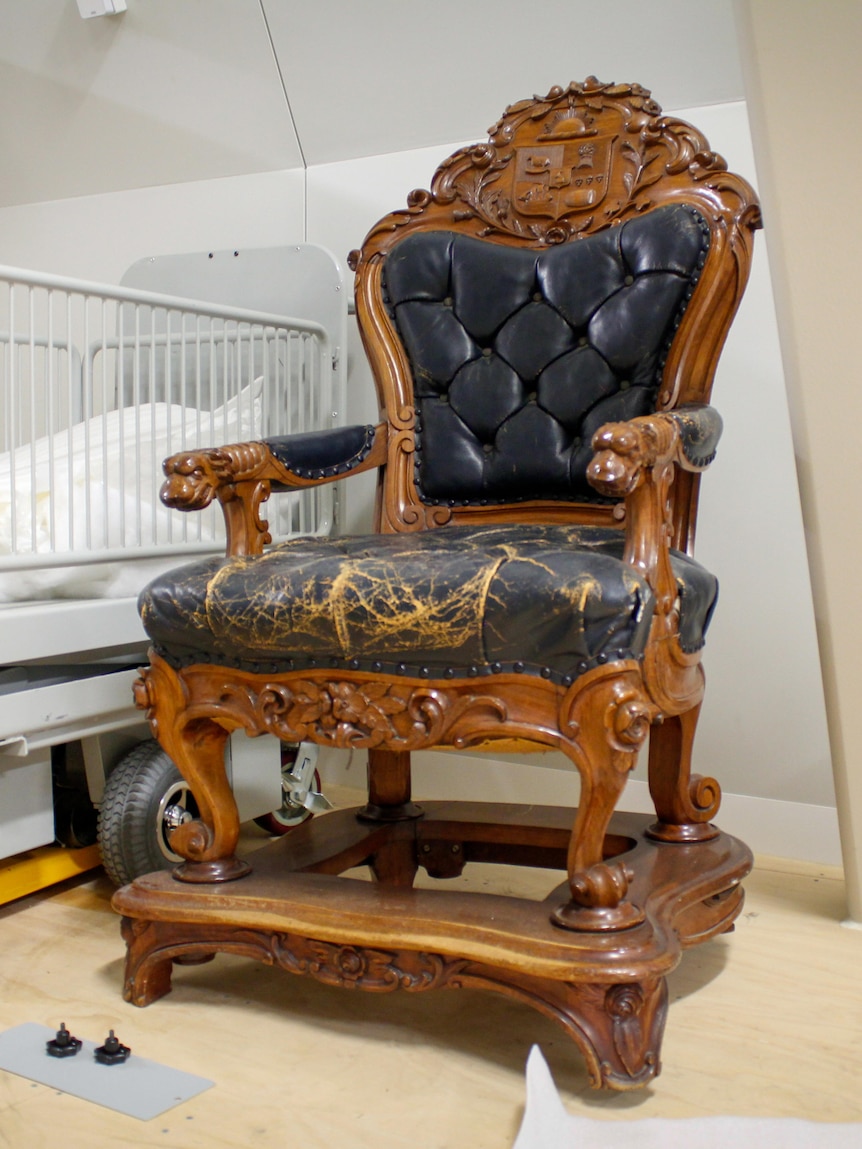 An ornate wooden chair with cracked blue leather sits atop a retrospectively build wooden platform