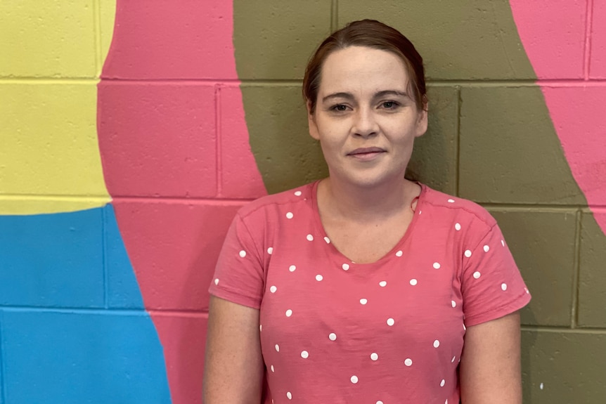 A woman in a pink shirt stands in front of a multi-coloured wall