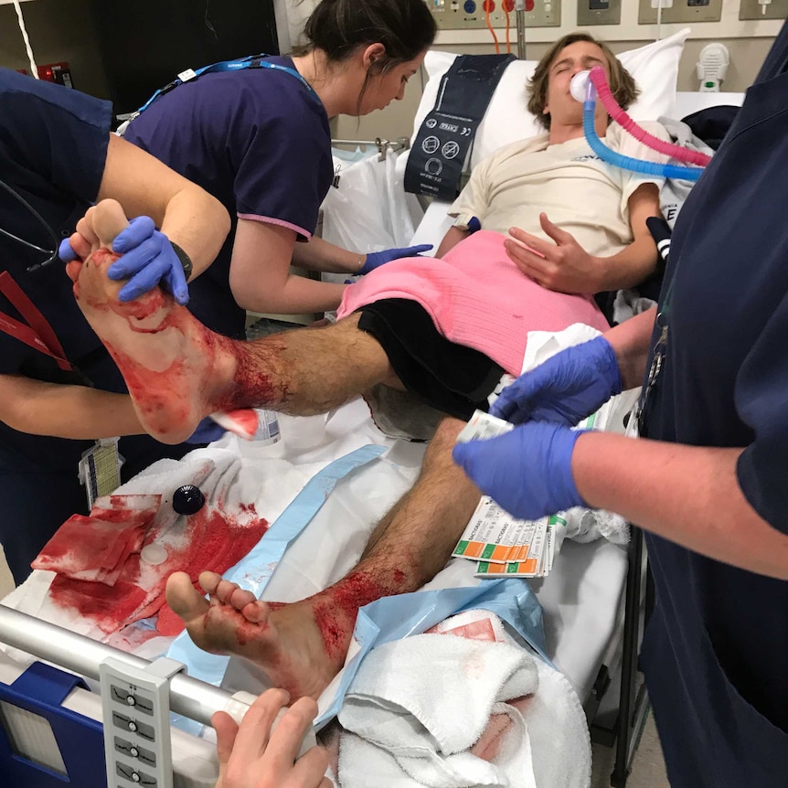 Sam Kanizay lies in a hospital bed as he is attended to by medical staff.