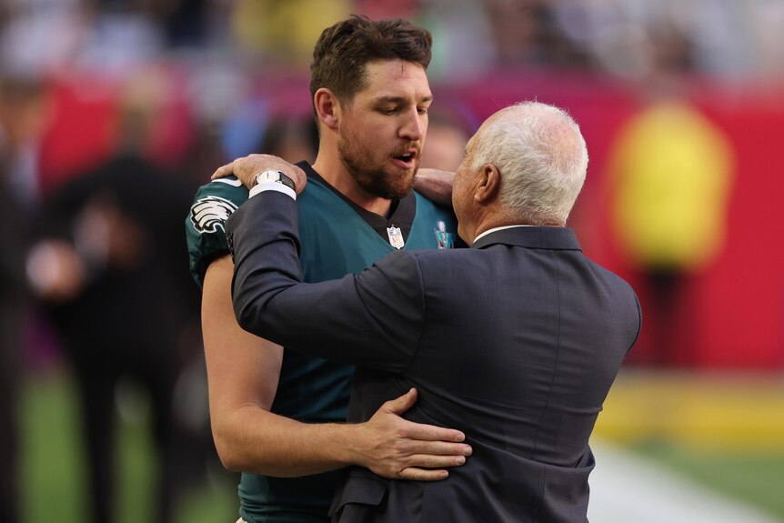 Philadelphia Eagles owner Jeffrey Lurie (back turned) hugs Australian NFL player Arryn Siposs before the Super Bowl.