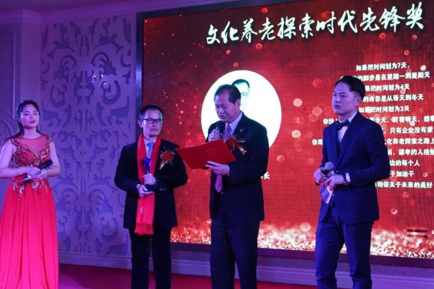 Three Chinese men in suits and one lady in a red evening gown present on stage.
