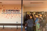 Warlpiri Aboriginal people gathered in the doorway of the police station, which has red hand prints on its wall