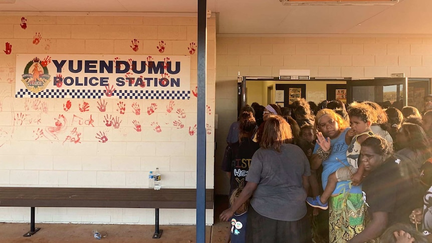 Warlpiri Aboriginal people gathered in the doorway of the police station, which has red hand prints on its wall