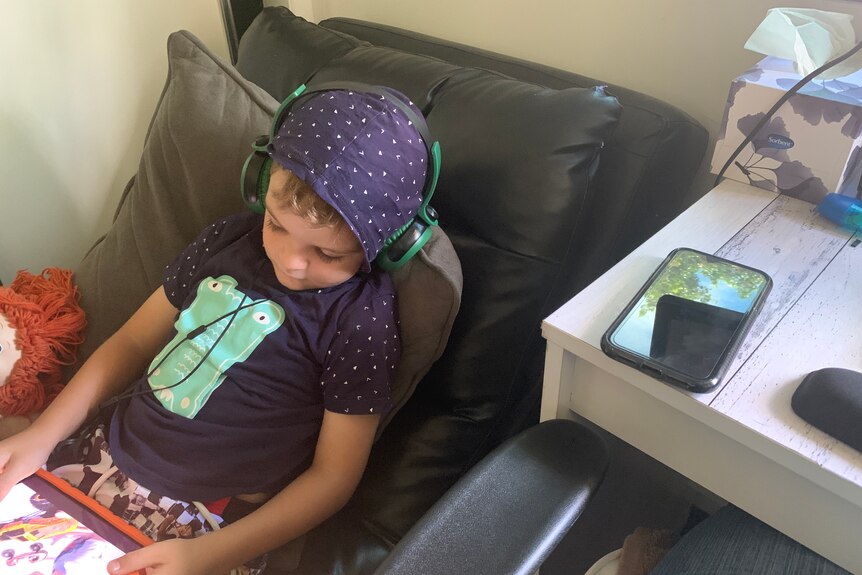 kid sits in chair with headphones in and watching ipad. 