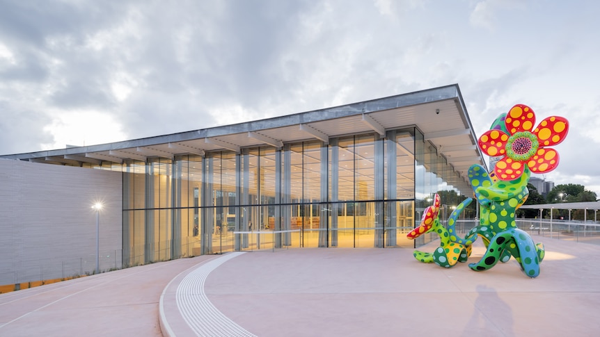 A large, brightly coloured sculpture of flowers stands outside a building lined with large windows