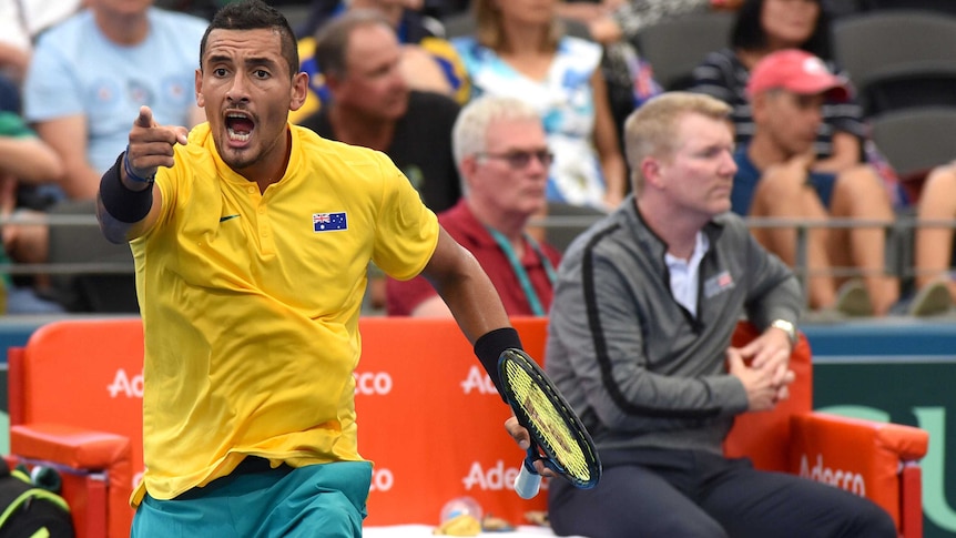 Nick Kyrgios, appearing angry, points at someone across the court.
