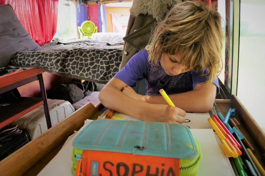 Girl, 8, in a campervan-style bus concentrating on drawing. Pencil case with name Sopia in marker.