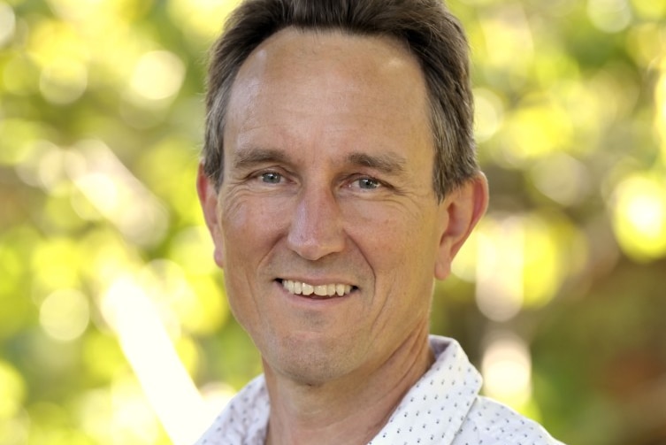 Peter Mares stands in front of trees wearing light shirt and smiling.