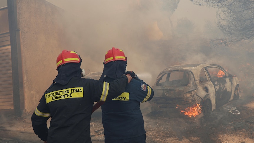 Two firefighters standing in front of a burned car and smoke. 