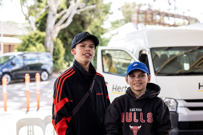 Two boys wearing caps standing next to each other and smiling.