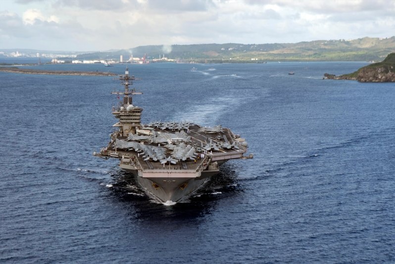 A very large aircraft carrier sails through the water carrying military aircraft.